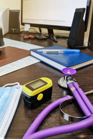 Stethoscope, face mask and pulse oximeter on the background of a notebook and a computer monitor - a...