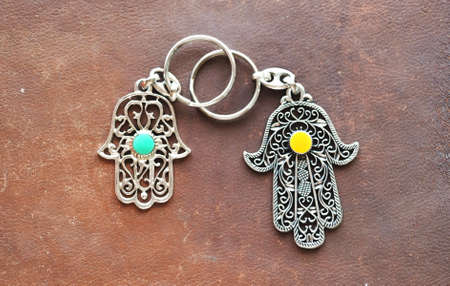 Two key rings in the form of Fatima Hand on a brown leather background. Ancient symbol and...
