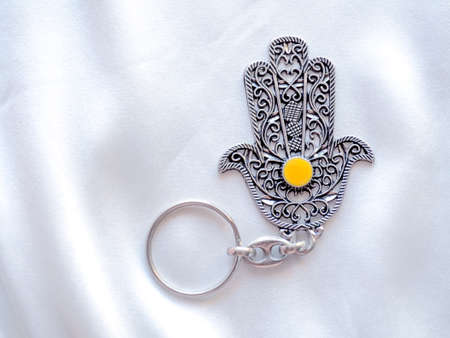 A key ring in the form of Fatima Hand on a white silk background. Ancient symbol and traditional modern tourist souvenir of Tunisiaの写真素材