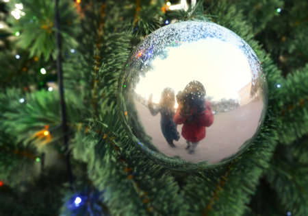 Reflection of two human figures in the Christmas ball on the branches of artificial firの写真素材
