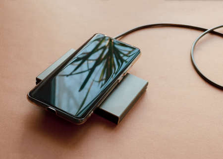 A phone is charging from a rectangular induction charger. Wireless chargerの写真素材