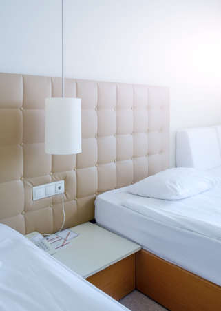 Sunny room in a hotel in light colors with two beds, bedside table and a lampの写真素材