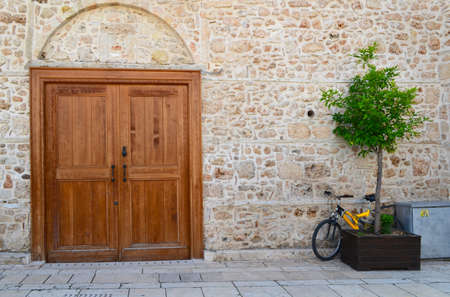 Yellow bicycle and tub with a tree against a stone wall with a large wooden doorの写真素材