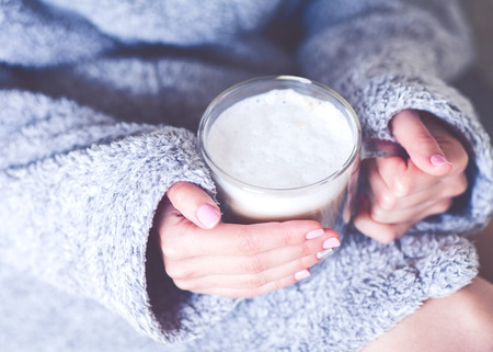 the girl is holding a mug of coffee in her hands in a gray dressing-gownの写真素材