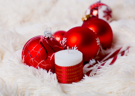 red christmas balls and decorated candle on a fur backgroundの写真素材