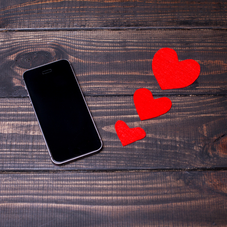 Black smart phone with blank screen lying on the wooden background with red hearts. Concept for Valentine's Dayの写真素材