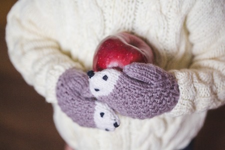kids hands in cozy mittens holding red appleの写真素材
