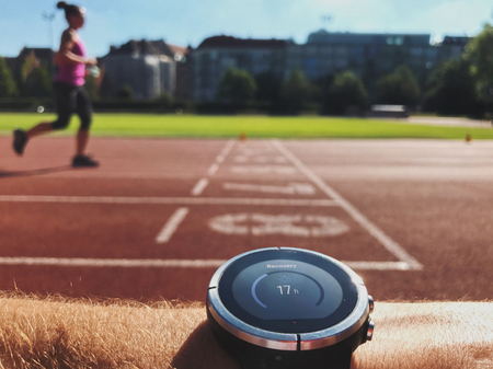 Trainer checking progress on smart watch. Female runner runnng on sport arenaの写真素材