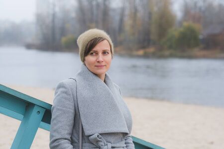 Young woman walking away alone on a river coast wearing a grey overcoat