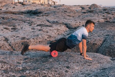 Man doing self massage of the body with a roll near the oceanの写真素材