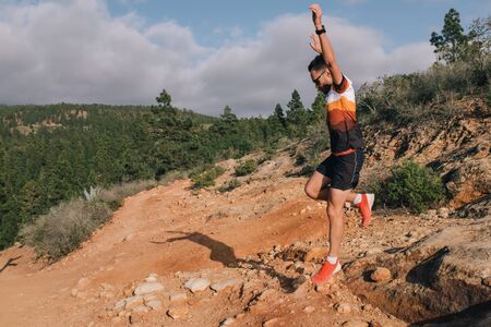 Sport running man in cross country trail run. Fit male runner exercise training and jumping outdoors in beautiful mountain nature landscapeの写真素材