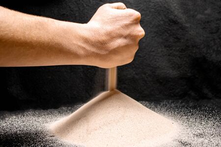 Sand pours from a hand on a black backgroundの写真素材
