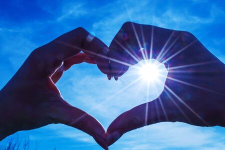 Through the fingers of a woman heart-shaped, the sun is outwardly against the skyの写真素材