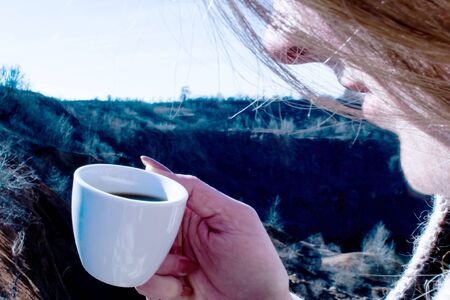 Woman holds morning coffee on sky and canyon backgroundの写真素材
