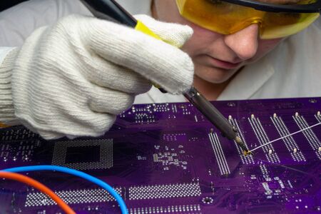 Female master solders a motherboard with a soldering iron