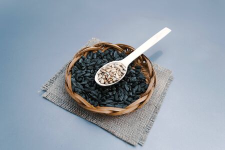 Sunflower seeds in a wicker plate, seeds in a wooden spoon on a brown napkin on a gray background