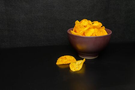 Chips in a clay plate and a glass of beer with foam on a black background