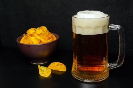 Chips in a clay plate and a glass of beer with foam on a black background