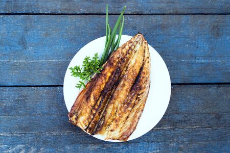 Baked mackerel fish on a white plate on a blue wooden tableの写真素材