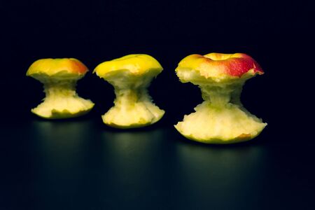 Apples with a pink side and a stub from an apple are laid out in a row on a black background.