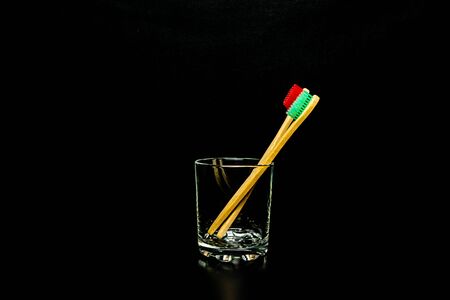 Dental and oral care products. Hygiene of teeth and oral cavity Two wooden toothbrushes in a glass cup on a black background.の写真素材