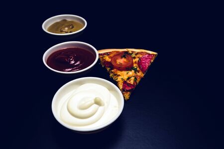 Slice of pizza, ingredients and sauces on a black background