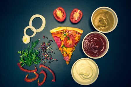 Slice of pizza, ingredients and sauces on a black backgroundの写真素材
