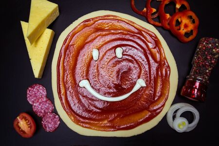 Dough base with ketchup and pizza ingredients, on black backgroundの写真素材