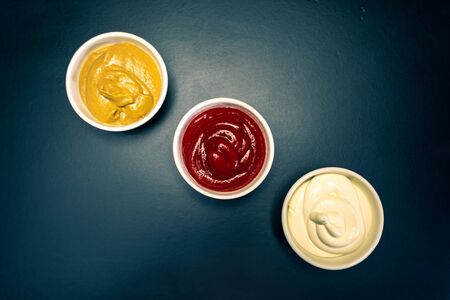 Ketchup, mayonnaise, mustard sauces on a black backgroundの写真素材