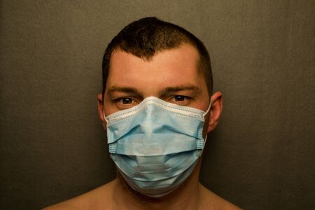 Man's face is covered with a medical mask, gray background