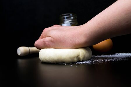 Hand kneads dough on a black background. Rolling pin, sunflower oil in the background