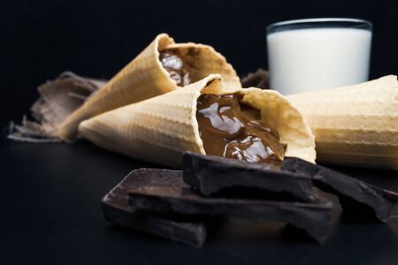 Wafer rolls with condensed milk, a glass of milk on a black backgroundの写真素材