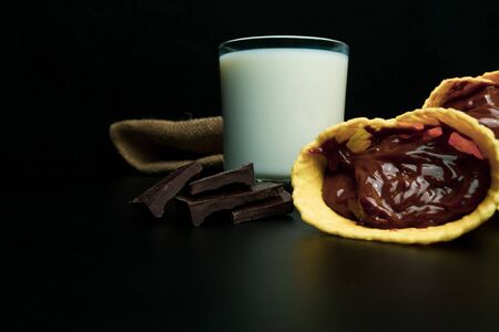 Wafer rolls with condensed milk, a glass of milk on a black backgroundの写真素材