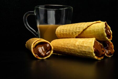 Wafer rolls with condensed milk and a cup of cocoa on a black backgroundの写真素材