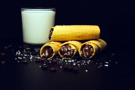 Wafer rolls with condensed milk, a glass of milk and coffee grains on a black backgroundの写真素材