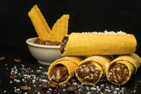 Wafer rolls with condensed milk and a saucer in which there is a filler for wafers on a black...