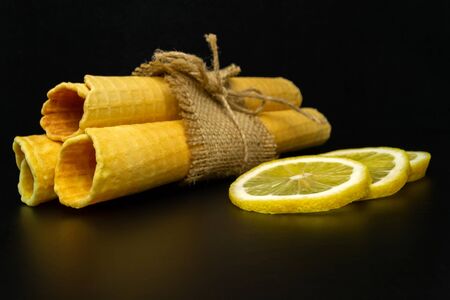 Wafer rolls with condensed milk and lemon on a black background