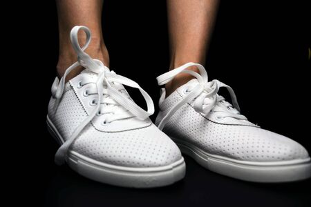 White sneakers are dressed on legs on a black background. Sport shoesの写真素材