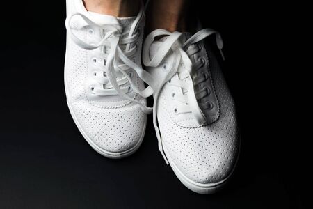 White sneakers are dressed on legs on a black background. Sport shoesの写真素材