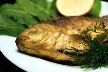 Grilled crucian on a white plate. Cooking fried fish. A dish of fried crucian carp. Tasty river fish. Grilled fish garnished with greensの写真素材