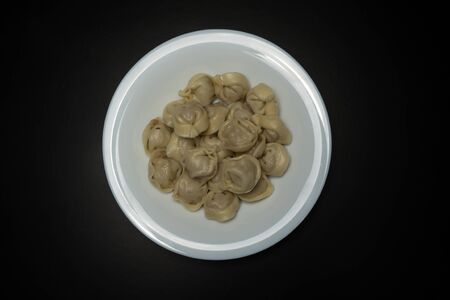 Tasty boiled homemade dumplings with minced meat in a white plate on a black backgroundの写真素材