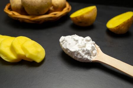 Sliced potatoes and a spoonful of starch on a black backgroundの写真素材