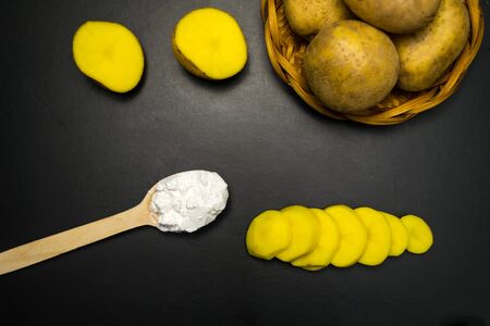 Sliced potatoes and a spoonful of starch on a black backgroundの写真素材