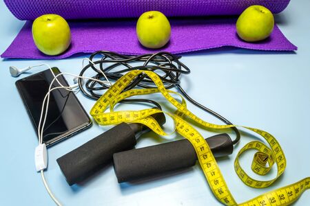 Yoga mat and glass of water close-up. Sports equipment, green apples and a jump rope.