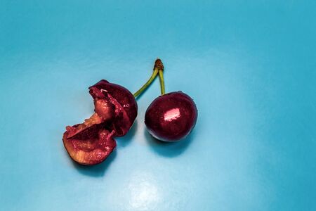 Two red ripe juicy cherries, one of which is bitten, blue backgroundの写真素材