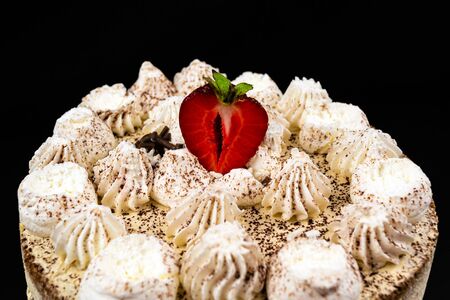 Tiramisu cake decorated with a slice of strawberries, on a black background. Close-upの写真素材
