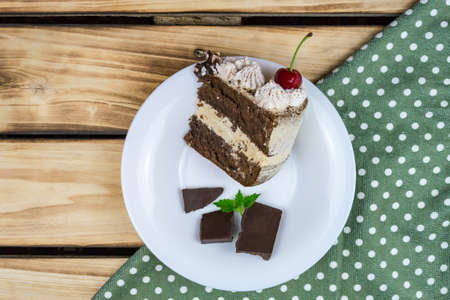 A triangular piece of tiramisu fell on a white plate, a piece of chocolate. Wood background