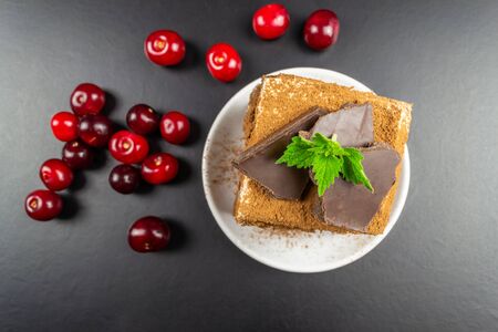Square piece of tiramisu on a white plate, decorated with chocolate. Black background.の写真素材