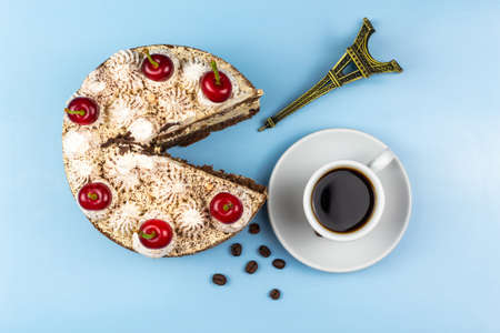 Tiramisu cake, cup of coffee, roasted coffee grains, Eiffel tower figurine. Blue background