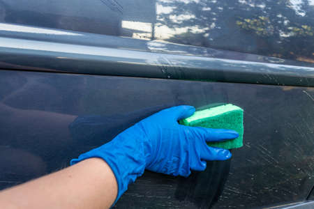 Car wash, woman in blue gloves and a sponge with foam wipes the car